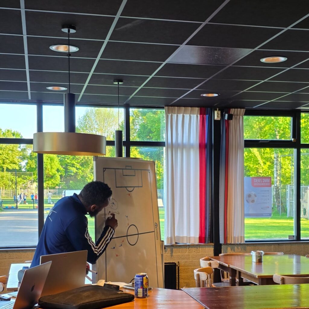 Overzicht van de ouderavond. De ouders luisteren aandachtig naar de uitleg van Shurell Wilson. Hij gebruikt een whiteboard om zijn tekst te verduidelijken.