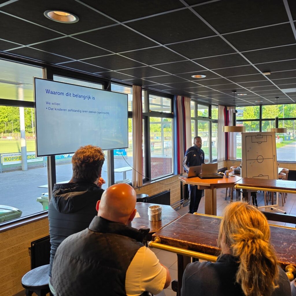 Overzicht van de ouderavond. De ouders luisteren aandachtig naar de uitleg van Shurell Wilson die voor de groep staat.