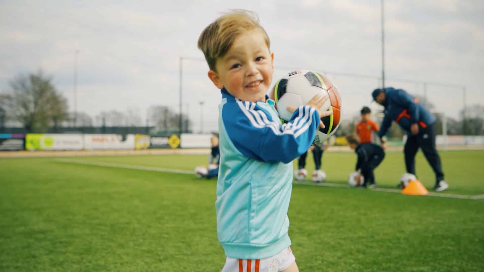 Lachende jongeman kijkt in de camera terwijl hij een voetbal vast heeft.